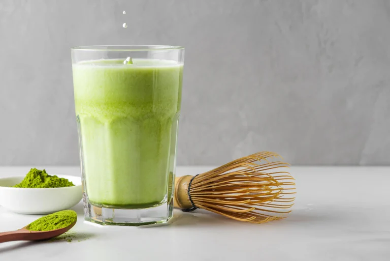 Matcha in a glass cup with a whisk and powder in a bowl